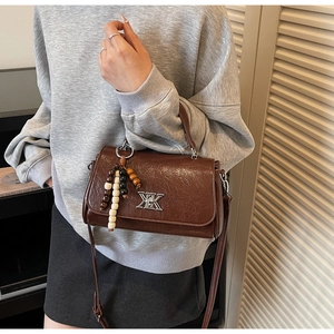 Détail d'un sac à bandoulière marron avec texture vintage et breloque en perles