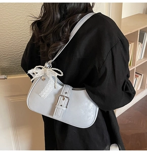 Détail d'un sac à bandoulière bleu demi-lune avec nœud en dentelle et chaîne de perles