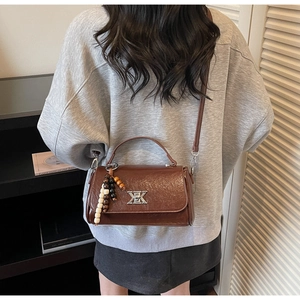 Détail du sac à main vintage en cuir plissé marron avec logo en métal et pompon perlé