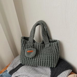 Détail du sac en tricot gris-vert montrant la texture épaisse et l'étiquette cœur en cuir