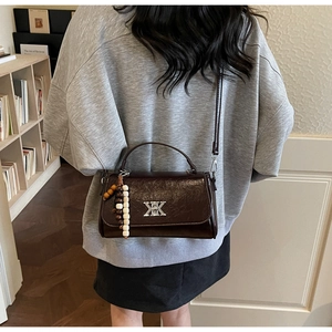 Détail du sac bandoulière en cuir verni marron foncé avec logo argenté et breloque