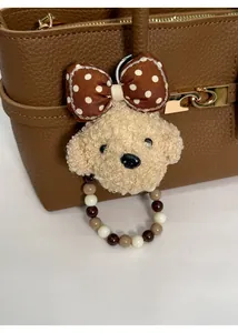 Detail of plush poodle bag charm with polka dot bow and beaded ring on brown handbag