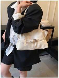 Detail view of beige shoulder bag with decorative metal buckle belt and silver eyelets