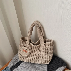 Détail du sac à main en maille beige avec une étiquette en cuir marquée Hand Made