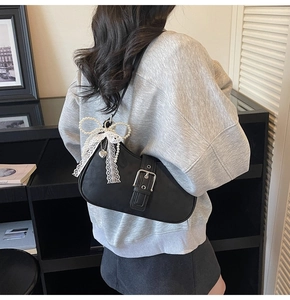 Détail du sac selle en cuir noir avec breloque nœud en perles et finitions en dentelle