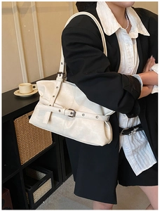 Detail of cream shoulder bag with leather strap buckle and textured finish on model