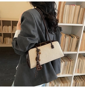 Detail shot of ivory canvas baguette bag with brown leather trim and vintage charms on shoulder