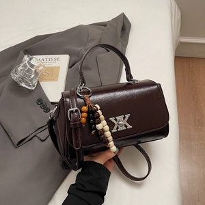 Détail d'un sac à main en cuir marron brillant avec boucle XK argentée et perle en bois