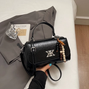 Détail d'un sac à main noir en cuir brillant avec boucle argentée et breloque perlée