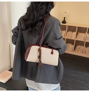 Detail view of beige canvas baguette bag with burgundy leather trim and knot fringe detail