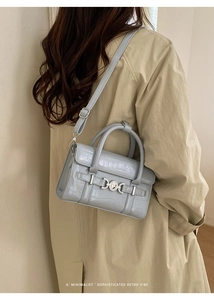 Dettaglio borsa celeste con trama a coccodrillo abbinata a un trench coat beige