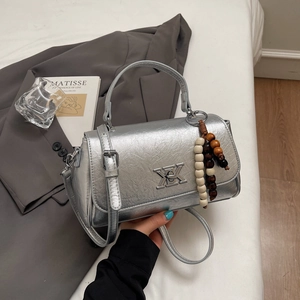 Détail du sac à main argenté à texture craquelée avec fermoir métal et pompon bois