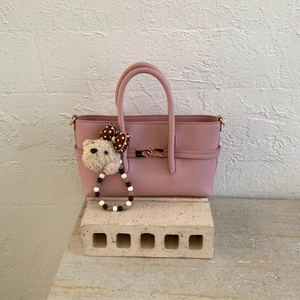 Detail of pink lychee leather handbag featuring a golden turn-lock and cute plush bear charm