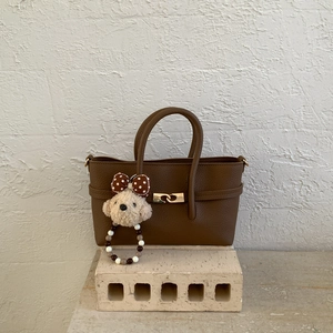 Close-up of brown pebbled leather handbag with gold metal clasp and plush bear charm