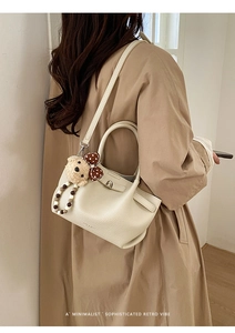 Close-up of beige textured leather bucket bag with cute teddy bear charm detail