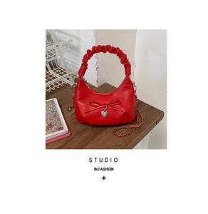 Close-up of red crescent bag with bow decoration, heart pendant, and chain strap