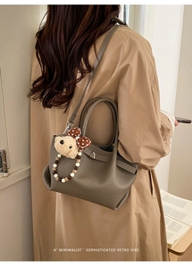 Detail of taupe pebbled leather bucket bag with plush bear charm and beaded strap decor