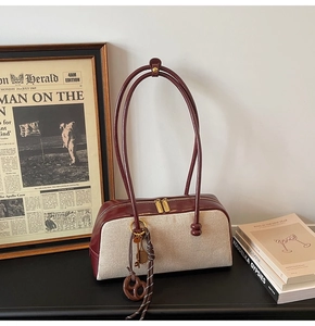 Detail view of canvas baguette bag with burgundy leather trim and golden accessories