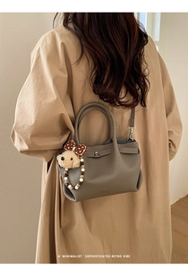 Detail of grey pebble leather bucket bag with metal turn-lock and cute bear charm