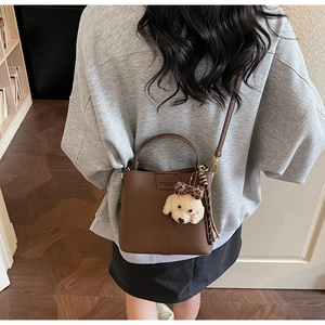 Dettaglio borsa a secchiello in pelle marrone scuro con ciondolo a forma di peluche