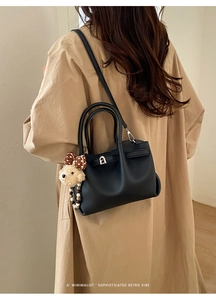 Detail of black pebbled leather bucket bag with silver lock and teddy bear charm on model