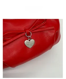 Close-up of red leather handbag detail featuring a silver heart pendant and bow