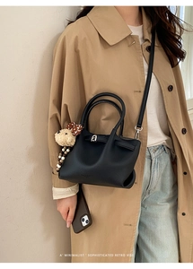 Detail of black lychee grain leather bucket bag with cute bear charm on a trench coat