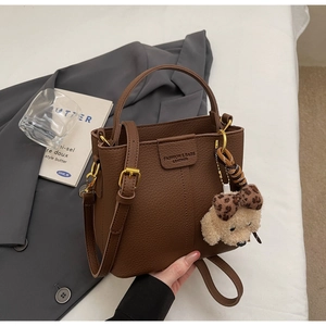 Dettaglio borsa a secchiello in pelle marrone scuro con trama litchi e ciondolo a cane di peluche