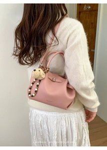 Detail of pink pebbled leather bucket bag featuring a cute dog charm and beaded chain strap