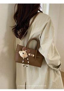 Macro view of brown lychee grain leather bag with a cute plush bear charm and beaded chain