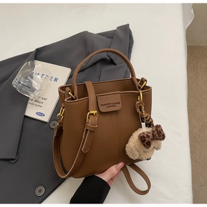 Dettaglio di una borsa a secchiello marrone con trama litchi e ciondolo a cucciolo