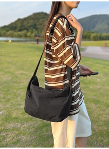 Outdoor view of a black water-resistant nylon messenger bag with adjustable wide strap