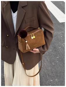 Detail einer braunen Wildleder-Kissentasche mit Plüschball und Fransen im Herbst-Outfit
