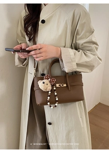 Detail of a brown leather tote bag featuring a gold twist lock and a cute teddy bear charm