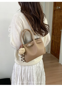 Detail of minimalist beige pebble leather bucket bag featuring cute bear charm and strap