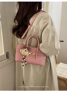 Detail shot of a pink pebbled leather baguette bag with golden clasp and plush bear charm