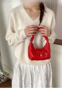 Detail of red crescent hobo bag featuring pleated handle and heart charm on soft leather