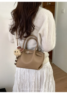 Detail of brown leather bucket bag with plush bear charm and metallic lock closure