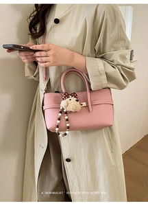 Pink lychee grain leather handbag detail with golden twist lock and plush puppy charm