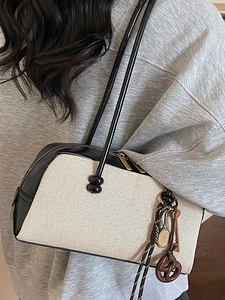 Large beige canvas baguette underarm bag with black leather trim and chic charms