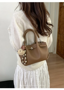 Close-up of brown litchi grain leather bucket bag with teddy bear and pearl charms