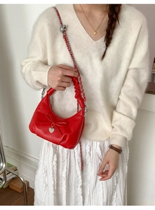 Red croissant bag with heart charm and bow detail worn on model with white outfit