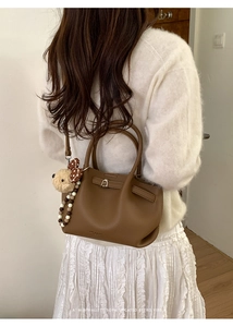 Detail view of brown pebbled leather bucket bag with plush dog charm and beaded chain