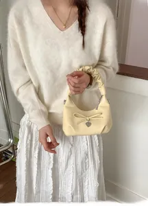 Detail of cream pleated handbag featuring a bow decoration and silver heart charm