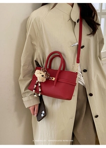 Detail of red lychee grain handbag with bear charm and polka dot bow on beige coat