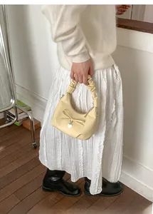 Detail of a creamy yellow small handbag with bow ornament, heart charm, and ruched handle