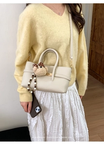 Close-up of minimalist beige leather baguette bag with plush teddy bear charm detail