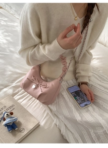 Detail view of pink bow shoulder bag with silver heart pendant and chain strap