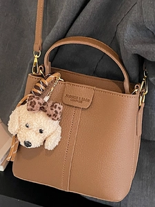 Borsa a secchiello in pelle marrone con ciondolo a cucciolo su sfondo cappotto grigio