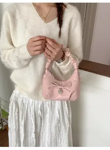 Pink PU leather handbag with ribbon bow and silver heart charm shown in lifestyle setting
